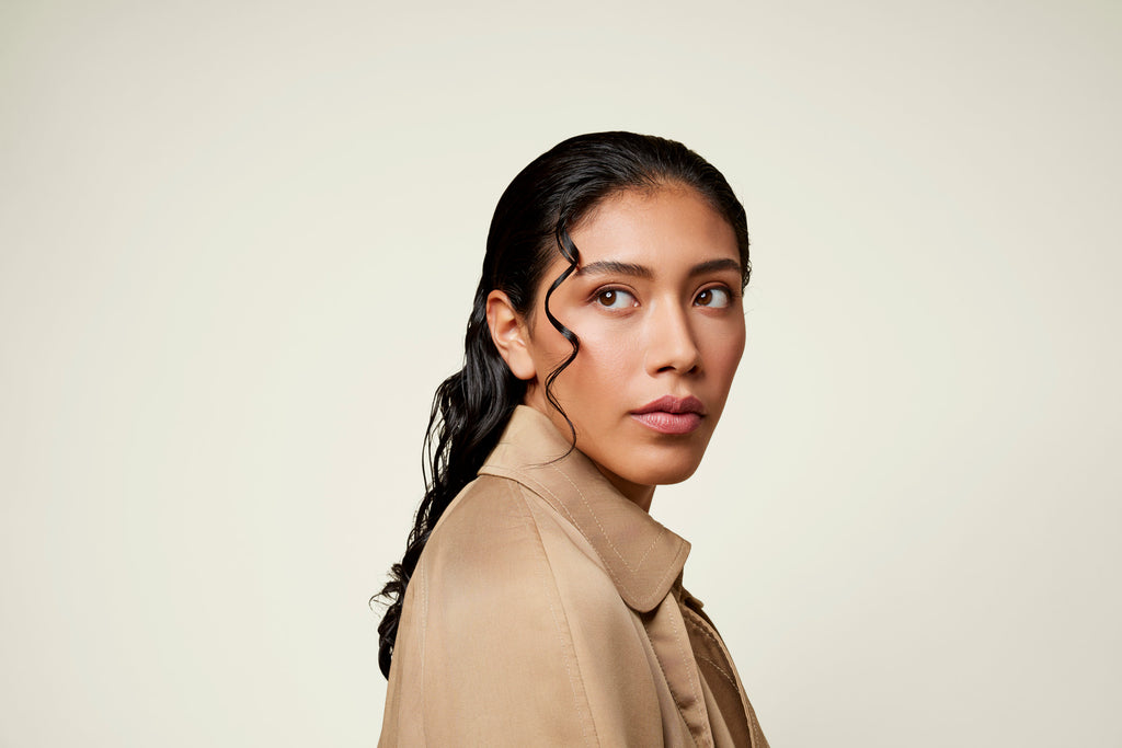 Woman in a trench coat with long, slicked-back curly hair