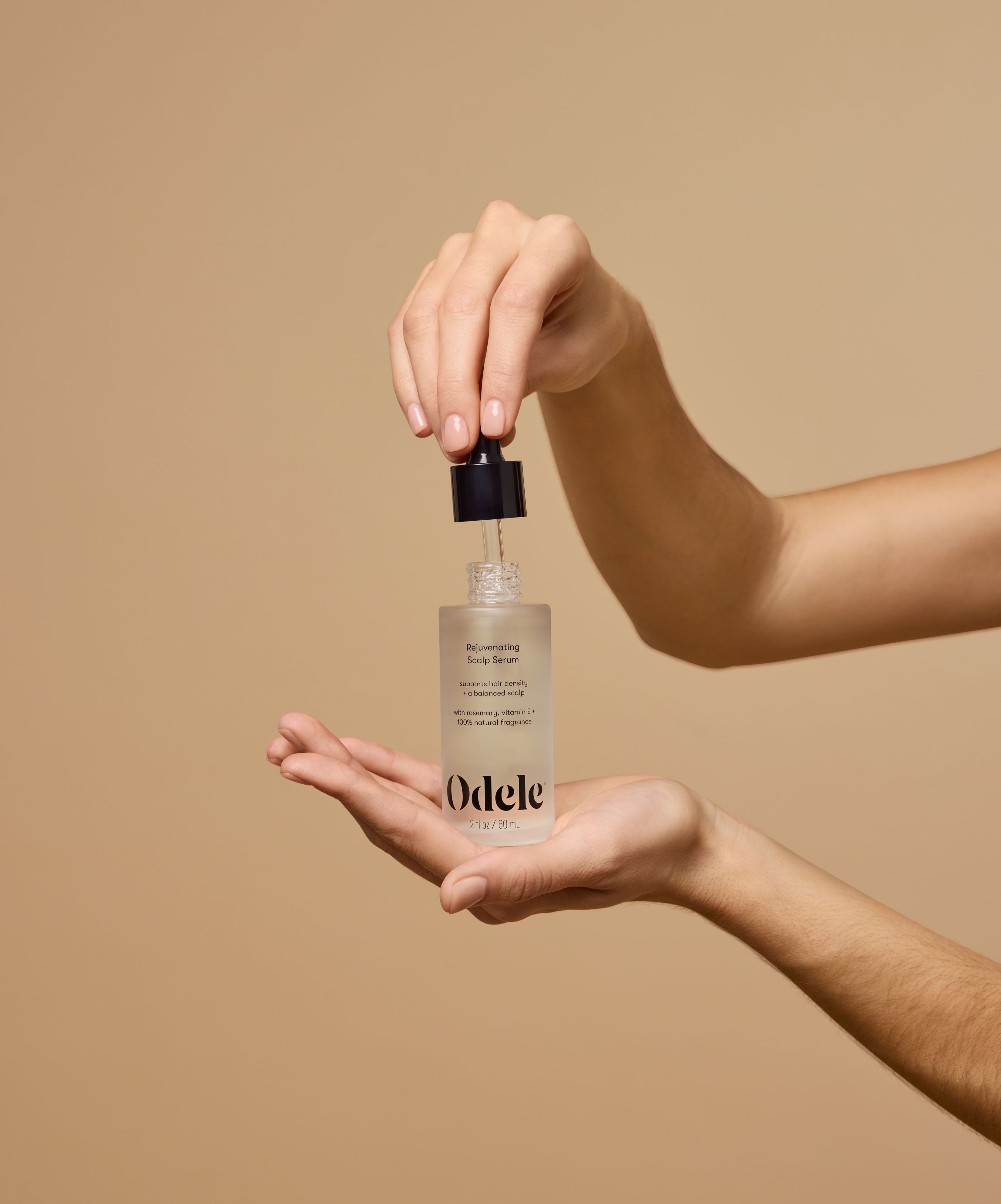 An unknown person holds the Odele Rejuvenating Scalp Serum in an outstretched palm as they lift the dropper from the bottle in front of a plain beige background.