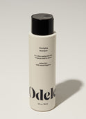 A bottle of Odele Clarifying Shampoo stands upright against a plain, light-colored backdrop with the front of the label facing the camera.