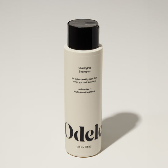 A bottle of Odele Clarifying Shampoo stands upright against a plain, light-colored backdrop with the front of the label facing the camera.