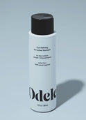 A bottle of Odele Curl Defining No-Lather Shampoo stands upright against a plain, light blue backdrop with the front of the label facing the camera.