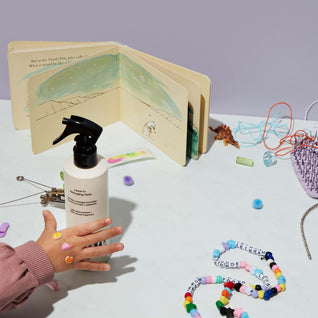 A child’s hand reaches for a bottle of Odele Leave-in Detangling Tonic that sits on a table strewn with beads, jewelry and other miscellaneous accessories.
