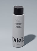 A bottle of Odele Moisture Repair Conditioner stands upright against a plain, light-colored backdrop with the front of the label facing the camera.
