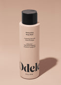A bottle of Odele Moisturizing Body Wash stands upright against a plain, light orange backdrop with the front of the label facing the camera.
