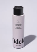 A bottle of Odele Purple Shampoo stands upright against a plain, light-colored backdrop with the front of the label facing the camera.