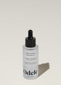 A bottle of Odele Rejuvenating Scalp Serum stands upright against a plain, light-colored backdrop with the front of the label facing the camera.