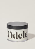 A jar of Odele Scalp & Body Scrub stands upright against a plain, light-colored backdrop with the front of the label facing the camera.