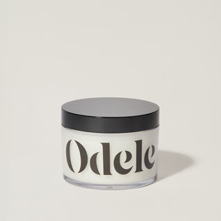 A jar of Odele Scalp & Body Scrub stands upright against a plain, light-colored backdrop with the front of the label facing the camera.