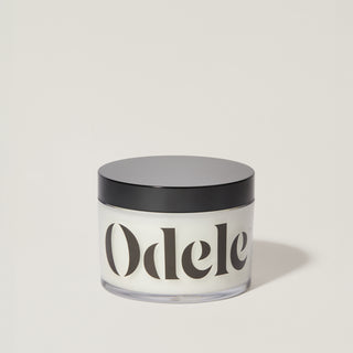 A jar of Odele Scalp & Body Scrub stands upright against a plain, light-colored backdrop with the front of the label facing the camera.