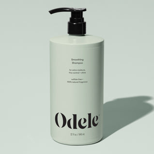 A light green bottle of Odele Smoothing Shampoo Bulk with a black pump, featuring benefits like extra moisture, frizz control, shine, sulfate-free formula, and natural fragrance, set against a pale green background.