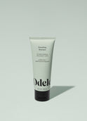 A tube of Odele Smoothing Shampoo stands upright against a plain, light green backdrop with the front of the label facing the camera.