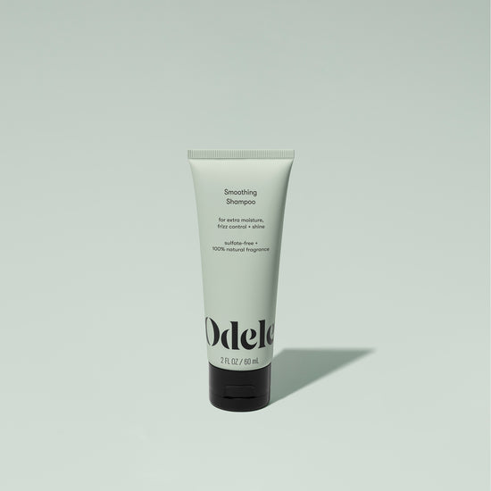 A tube of Odele Smoothing Shampoo stands upright against a plain, light green backdrop with the front of the label facing the camera.