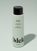 A bottle of Odele Smoothing Conditioner stands upright against a plain light green backdrop with the front of the label facing the camera.