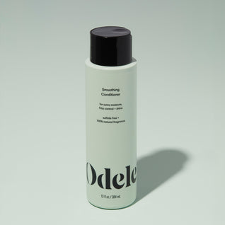 A bottle of Odele Smoothing Conditioner stands upright against a plain light green backdrop with the front of the label facing the camera.