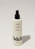 A bottle of Odele Texturizing Sea Salt Spray stands upright against a plain, light-colored backdrop with the front of the label facing the camera.