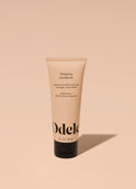 A tube of Odele Thickening Conditioner stands upright against a plain, light orange backdrop with the front of the label facing the camera.