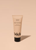 A tube of Odele Thickening Shampoo stands upright against a plain, light orange backdrop with the front of the label facing the camera.