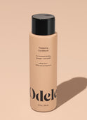 A bottle of Odele Thickening Conditioner stands upright against a plain, light orange backdrop with the front of the label facing the camera.