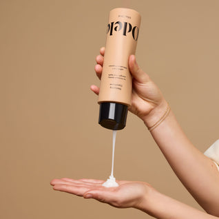 A hand dispenses Odele Thickening Conditioner onto an outstretched palm against a plain beige background.