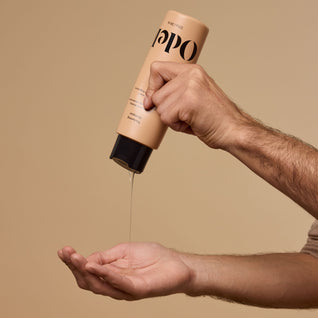 A male hand dispenses Odele Thickening Shampoo onto an outstretched palm against a plain beige background.
