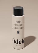 A bottle of Odele Ultra Sensitive Shampoo stands upright against a plain, light-colored backdrop with the front of the label facing the camera.