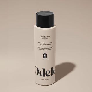 A bottle of Odele Ultra Sensitive Shampoo stands upright against a plain, light-colored backdrop with the front of the label facing the camera.