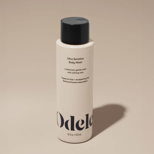 A bottle of Odele Ultra Sensitive Body Wash stands upright against a plain, light-colored backdrop with the front of the label facing the camera.