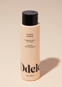 A bottle of Odele Volumizing Conditioner stands upright against a plain, light orange backdrop with the front of the label facing the camera.