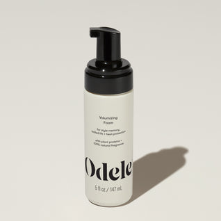 A bottle of Odele Volumizing Foam stands upright against a plain light-colored backdrop with the front of the label facing the camera.