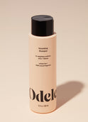 A bottle of Odele Volumizing Shampoo stands upright against a plain, light orange backdrop with the front of the label facing the camera.
