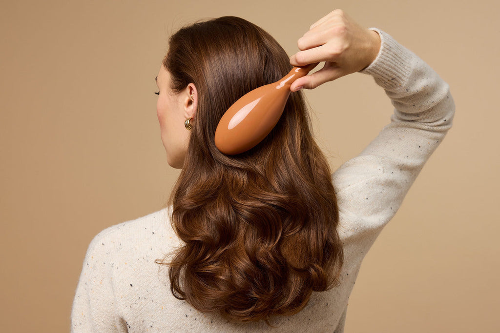 A person runs a brush through their full, wavy brown hair.