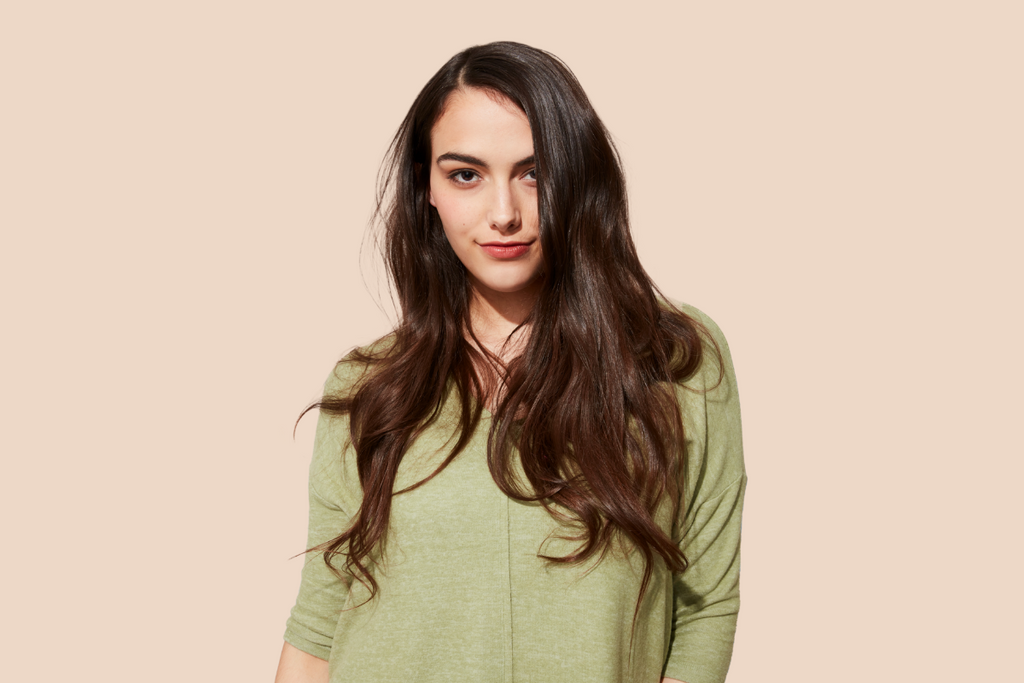 A person with shiny, smooth long brown hair wearing green pajamas stands against a plain beige background.