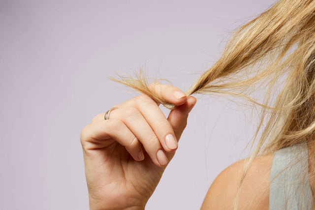 Woman holds a tuft of medium-length blonde hair between her fingers.