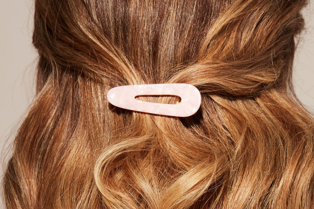 Closeup of red, wavy hair with a pink barrette.