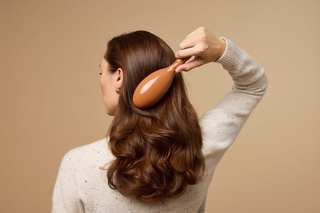 A woman runs a brush through her long, wavy brown hair