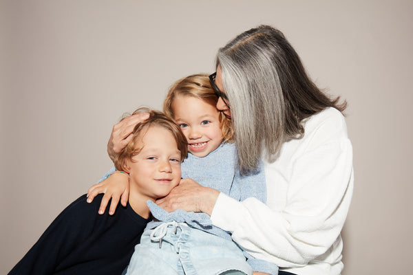 An older woman with gray hair hugs two young children