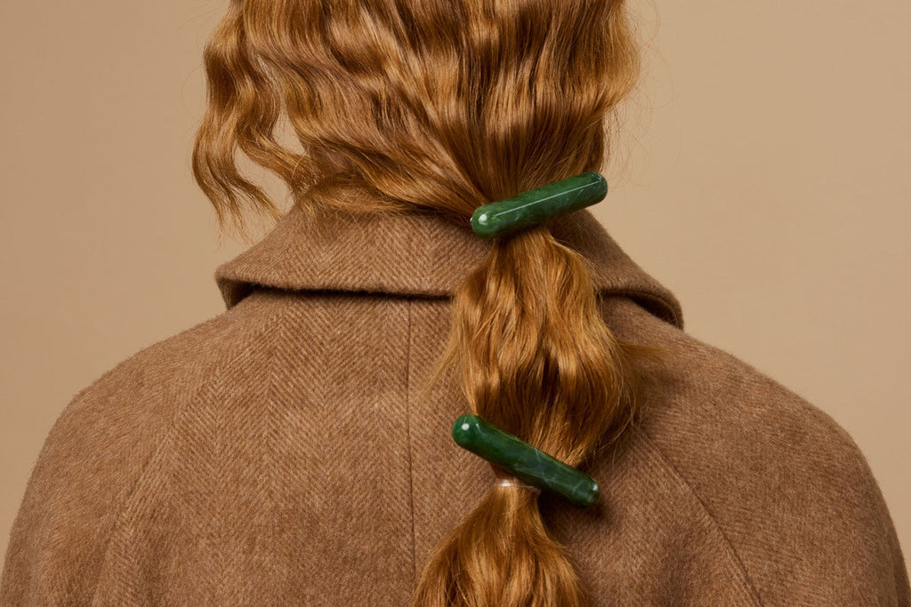 Back view of a person with wavy honey-blonde hair secured with two green barrette clips