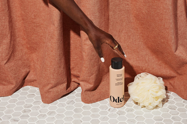 A hand reaches for a bottle of Odele Moisturizing Body Wash and loofah