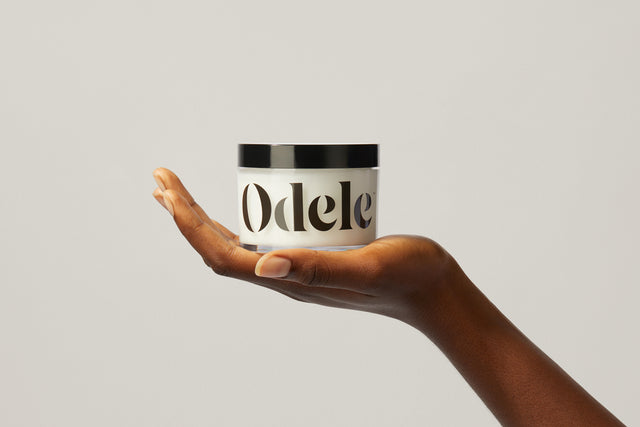 A hand holds up a jar of Odele Scalp and Body Scrub