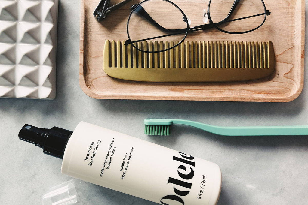 Odele Texturizing Sea Salt Spray on a surface next to a toothbrush, comb and glasses
