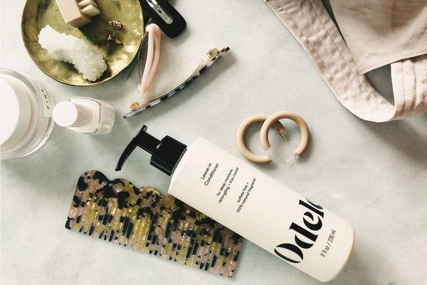 A bottle of Odele Leave-in Conditioner laying on a surface among hair clips and other accessories