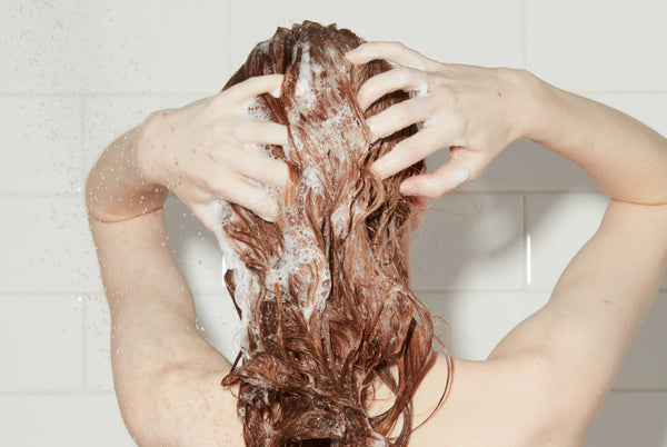 Woman in shower lathers shampoo into her long, red hair