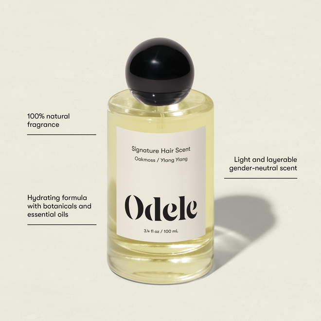 A clear bottle of Signature Hair Scent with a black cap, labeled “Oakmoss / Ylang Ylang.” Its 100% natural fragrance blends cucumber and bamboo for a hydrating, light, gender-neutral scent like fresh outdoor air.