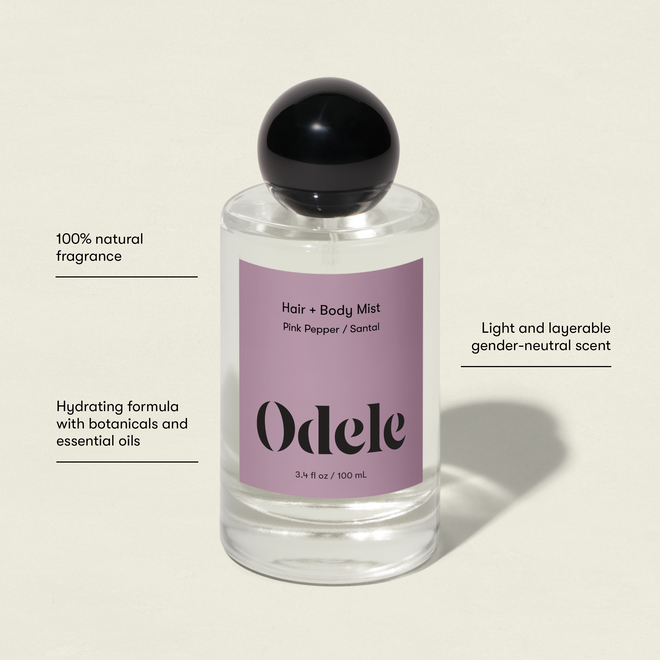 A clear glass bottle of Odele Hair + Body Mist, featuring a black cap and pink label. Showcases its natural fragrance, hydrating botanicals, and a light, gender-neutral sandalwood scent ideal for layering.