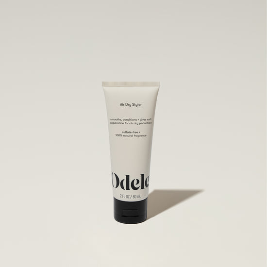 A tube of Odele Air Dry Styler stands upright against a plain, light-colored backdrop with the front of the label facing the camera.