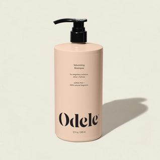 A beige bottle of Volumizing Shampoo Bulk with a black pump sits on a light background. The label highlights its salon-grade volume, weightless moisture, and 100% natural fragrance.
