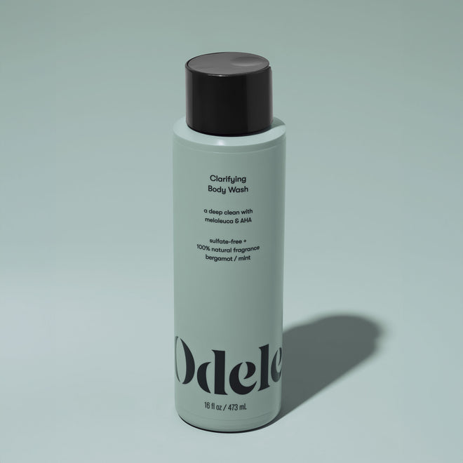 A bottle of Odele Clarifying Body Wash stands upright against a plain, light green backdrop with the front of the label facing the camera.