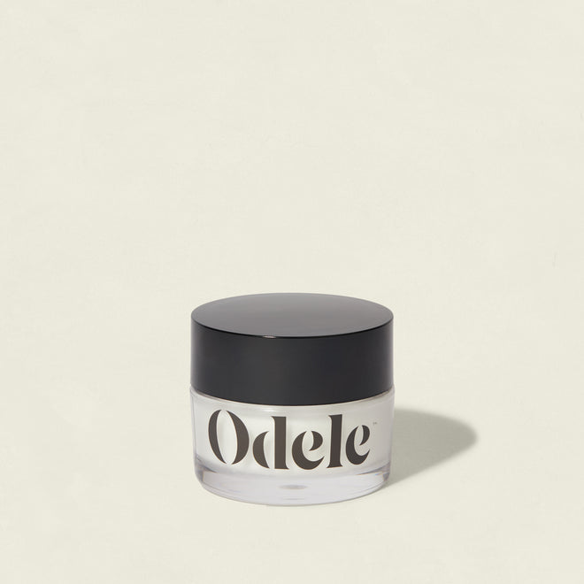 A clear jar labeled Odele with a black lid sits on a light background. The Cream Pomade offers flexible hold and a natural finish, casting a soft shadow to the right.