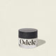 A clear jar labeled Odele with a black lid sits on a light background. The Cream Pomade offers flexible hold and a natural finish, casting a soft shadow to the right.