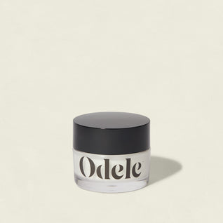A clear jar labeled Odele with a black lid sits on a light background. The Cream Pomade offers flexible hold and a natural finish, casting a soft shadow to the right.